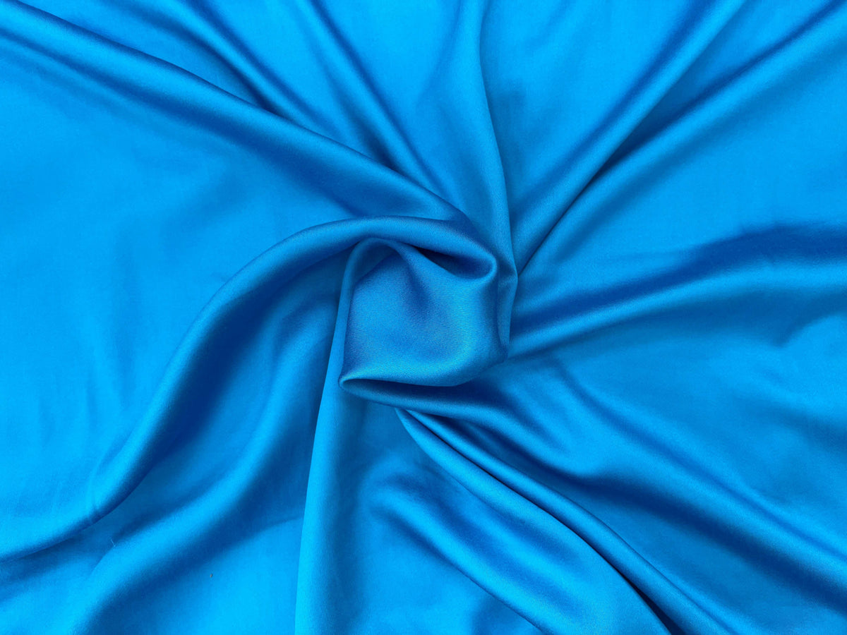 Smooth plain viscose satin fabric in kingfisher blue, showcasing its glossy, lightweight texture ideal for elegant garments.